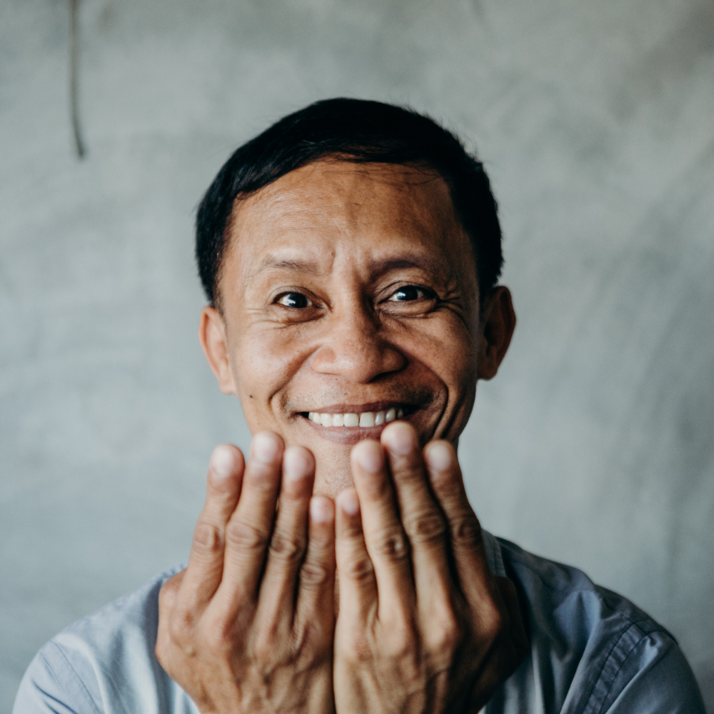 Smiling man holding hands in front of face.